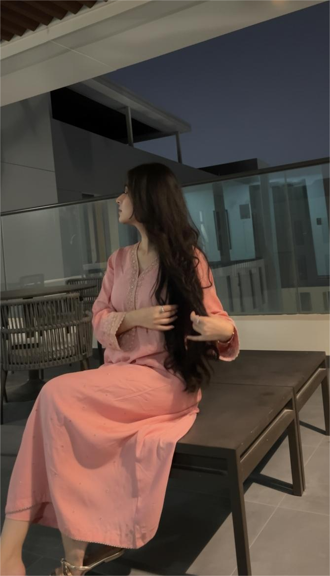 A woman with long hair and a floral dress sits with her hand on her head, 
        surrounded by soft pink and red fabric in the foreground.